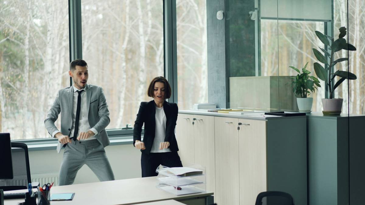 Joyful couple of colleagues is dancing in office having fun together moving arms and body relaxing after work. Millennials, carefree youth lifestyle and joy concept.