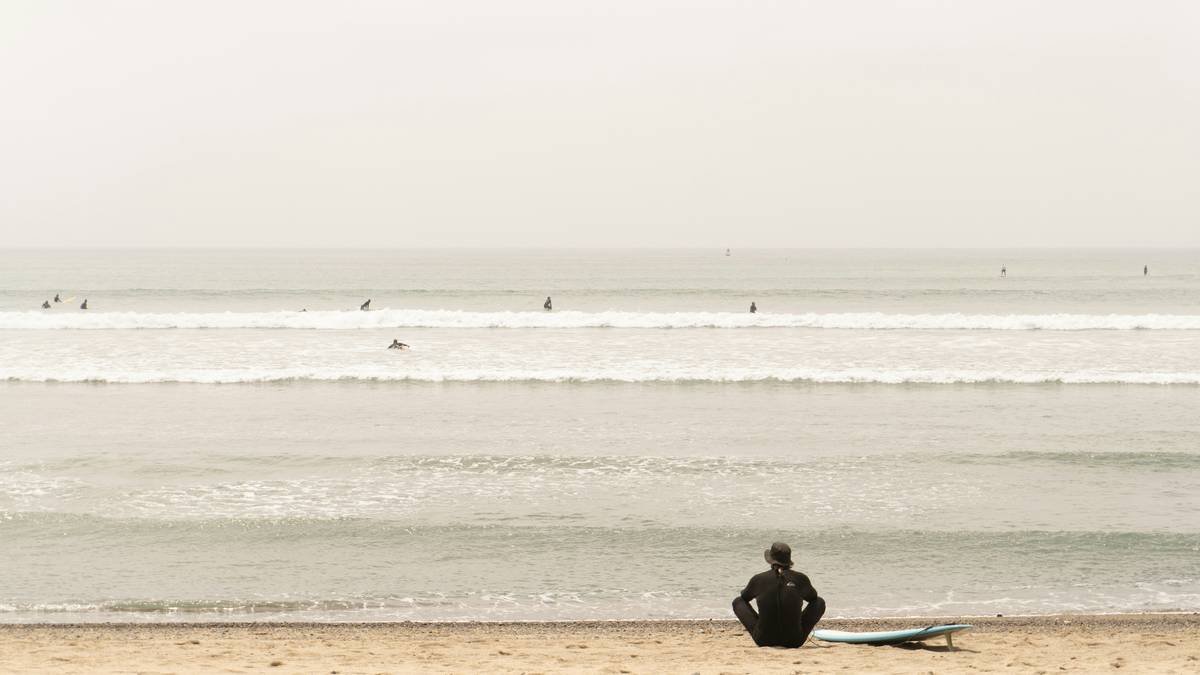 Surfer on beach looking at waves on a cloudy day.
